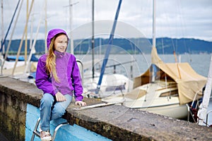 Little girl admiring beautiful yachts in a harbor of Lindau, a town on the coast of Bodensee lake in Germany on cloudy autumn day