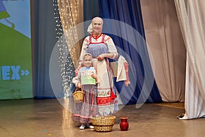 A little girl and an adult woman in Russian national dress posing with a diploma on stage after performing and winning the