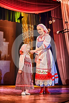 A little girl and an adult woman in Russian national dress rehearsing on stage. Mother and daughter sing and dance together