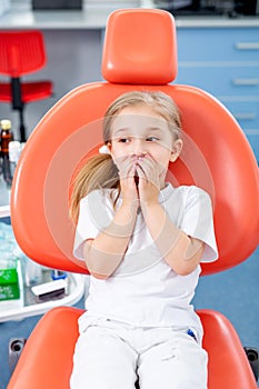 Little girl is afraid to show her teeth to a pediatric dentist. child girl in white clothes at reception at a pediatric dentist