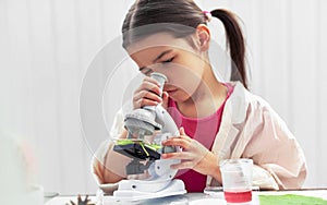 Little girl analyzing with microscope and exploring plants. The kid learning science in the school laboratory. Child looking on