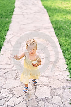 Little girl with an apple in her hand walks along a cobbled path in the green grass. View from above