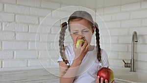 Little girl with apples in the kitchen. Child bites eating an apple