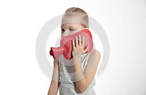 A little girl applies a heating pad with warm water to her neck for neck pain and toothache. Heat treatment