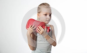 A little girl applies a heating pad with warm water to her shoulder joint for a sprained ligament. Heat treatment, close