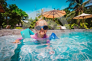 Little girl with armbands learn to swim in swimming pool