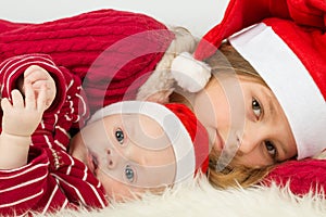 Little girl with baby boy lie in the hats of Santa Claus