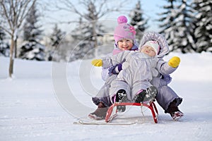 Little girl and baby dressed near forest sit on red sled