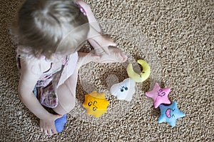 Little girl baby girl playing with handmade felt toys on the beige carpet. Educational toys. Toy sun, clouds, stars and moon.