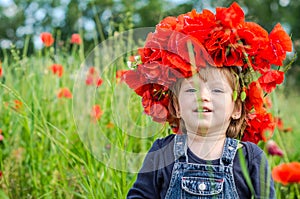 Little girl baby playing happy on the poppy field with a wreath, a bouquet of color A red poppies and white daisies, wearing a den