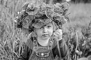 Little girl baby playing happy on the poppy field with a wreath, a bouquet of color A red poppies and white daisies, wearing a den