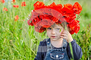 Little girl baby playing happy on the poppy field with a wreath, a bouquet of color A red poppies and white daisies, wearing a den