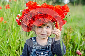 Little girl baby playing happy on the poppy field with a wreath, a bouquet of color A red poppies and white daisies, wearing a den