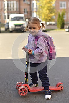 A little girl with a backpack riding a scooter.