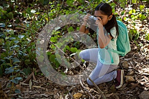 Little girl with backpack taking photo with camera on a sunny day