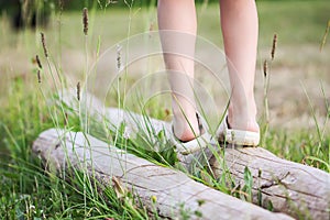 Little girl balancing on a log in summer park. Child& x27;s legs and green grass close up.