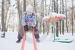 Little girl balancing on winter playground seesaw