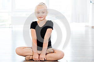 Little girl ballerina sitting with legs crossed in ballet studio