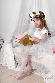 A little girl in a ballet dancer's fluffy skirt, sitting on a canopy bed and read