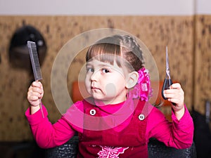 Little girl in barbershop with scissors and comb