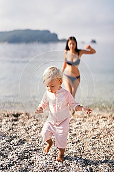 Little girl in a bathing suit walks barefoot on a pebbly beach