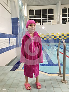 little girl in a bathrobe and a bathing cap after classes in the pool