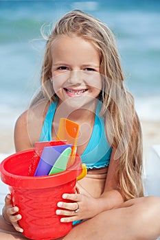 Little girl on the beach with small bucket and shovels for sand