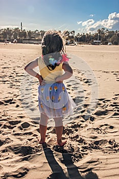 Little girl at beach, summer dressed child girl stands on sand looking far