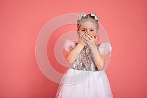 Little girl in a beautiful dress closes her mouth with her hands holding back a laugh