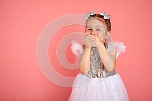 Little girl in a beautiful dress closes her mouth with her hands holding back a laugh