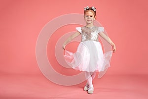 Little girl in a beautiful dress dancing over a pink background in the studio.