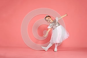 Little girl in a beautiful dress dancing over a pink background in the studio.