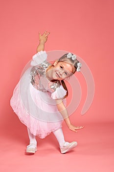 Little girl in a beautiful dress dancing over a pink background in the studio.