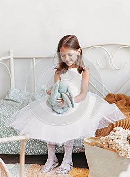 Little girl in a beautiful dress plays on the bed with a soft toy