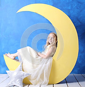 Little girl in a beautiful dress sits on a crescent moon.