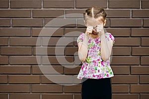 A little girl with a beautiful hairstyle is very upset and cries, wiping her eyes with her hands