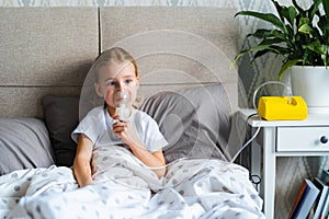 Little girl in bed using nebulizer or inhaler, child making inhalation at home