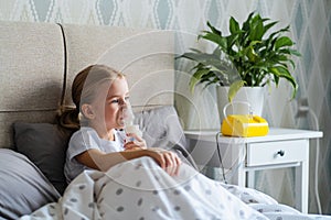 Little girl in bed using nebulizer or inhaler, child making inhalation at home