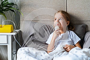 Little girl in bed using nebulizer or inhaler, child making inhalation at home