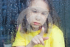a little girl behind a rain-splattered window
