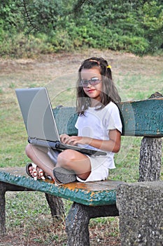 Little girl on a bench with computer and glasses