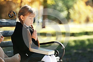 Little girl with Bible praying on bench outdoors