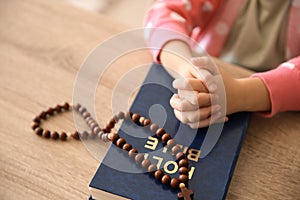 Little girl with Bible praying at wooden table
