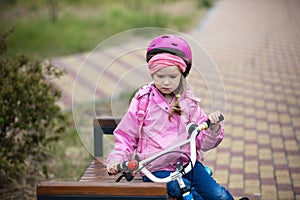 Little girl with bicycle looking upset, sitting on bench
