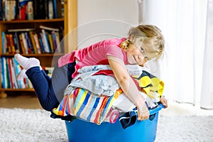 Little girl with a big basket of fresh clean laundry ready for ironing. Happy beautiful toddler and baby daughter