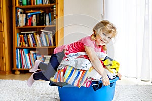 Little girl with a big basket of fresh clean laundry ready for ironing. Happy beautiful toddler and baby daughter