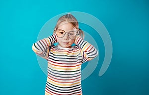 a little girl in big glasses covers her ears with her hands on an isolated blue background