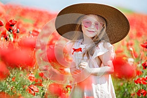 Little girl in big hat on a field of blooming red poppies