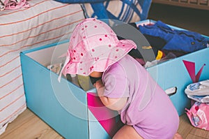 Little girl in a big purple hat looking for something in a big blue box