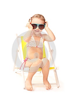 Little girl in big sunglasses sitting on deckchair